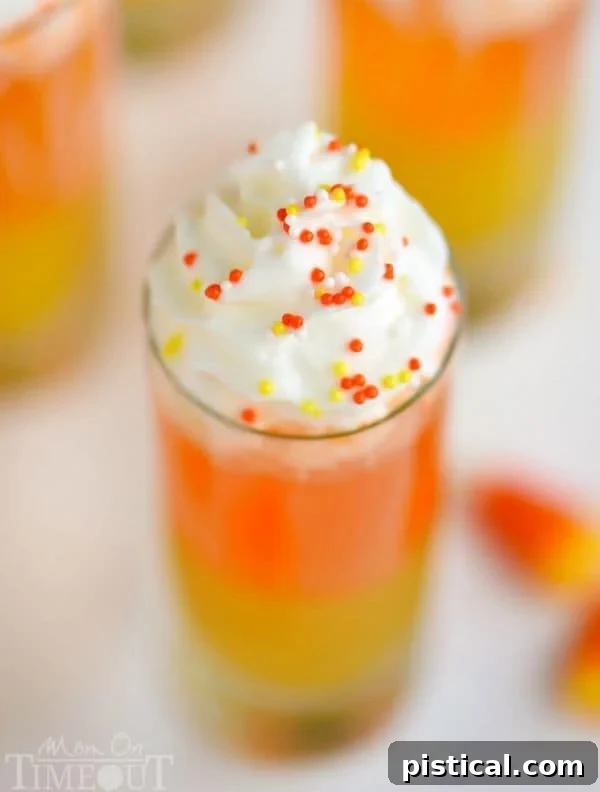 Candy Corn Nibbles 4 Overhead shot of Candy Corn Poppers in shot glasses on a rustic wooden surface, garnished with whipped cream and colorful sprinkles.