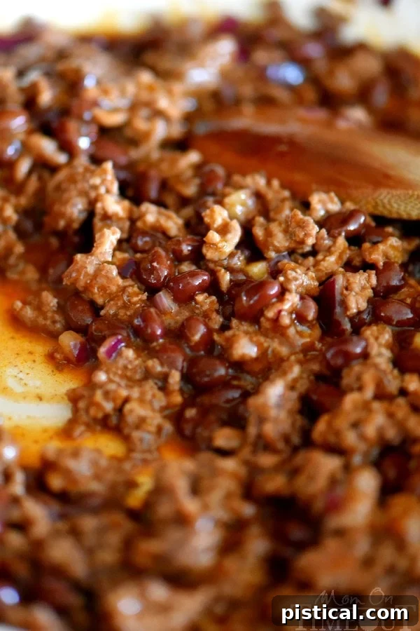 Close-up view of the savory beef, black bean, and diced onion mixture simmering in enchilada sauce in a skillet