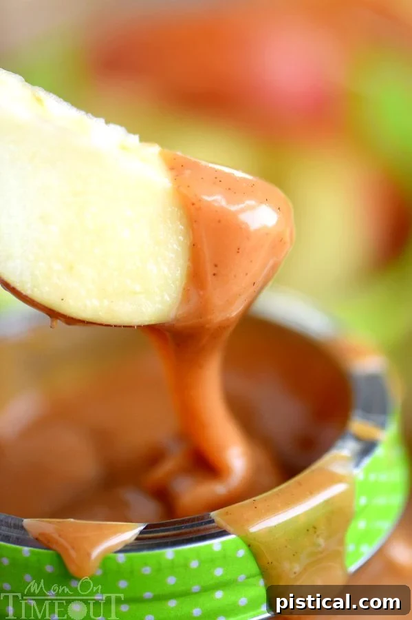 This easy Pumpkin Spice Caramel Apple Dip is sure to be the star at your next party! So easy to make and just bursting with fall flavor! Great for a fruit dip or as an ice cream topping! // Mom On Timeout #caramelappledip #caramelapple #pumpkinspice #pumpkin #thanksgiving #fall #holidays #appetizer #dip #recipe A crisp green apple being generously dipped into a creamy, spiced caramel apple dip, showcasing its rich texture.