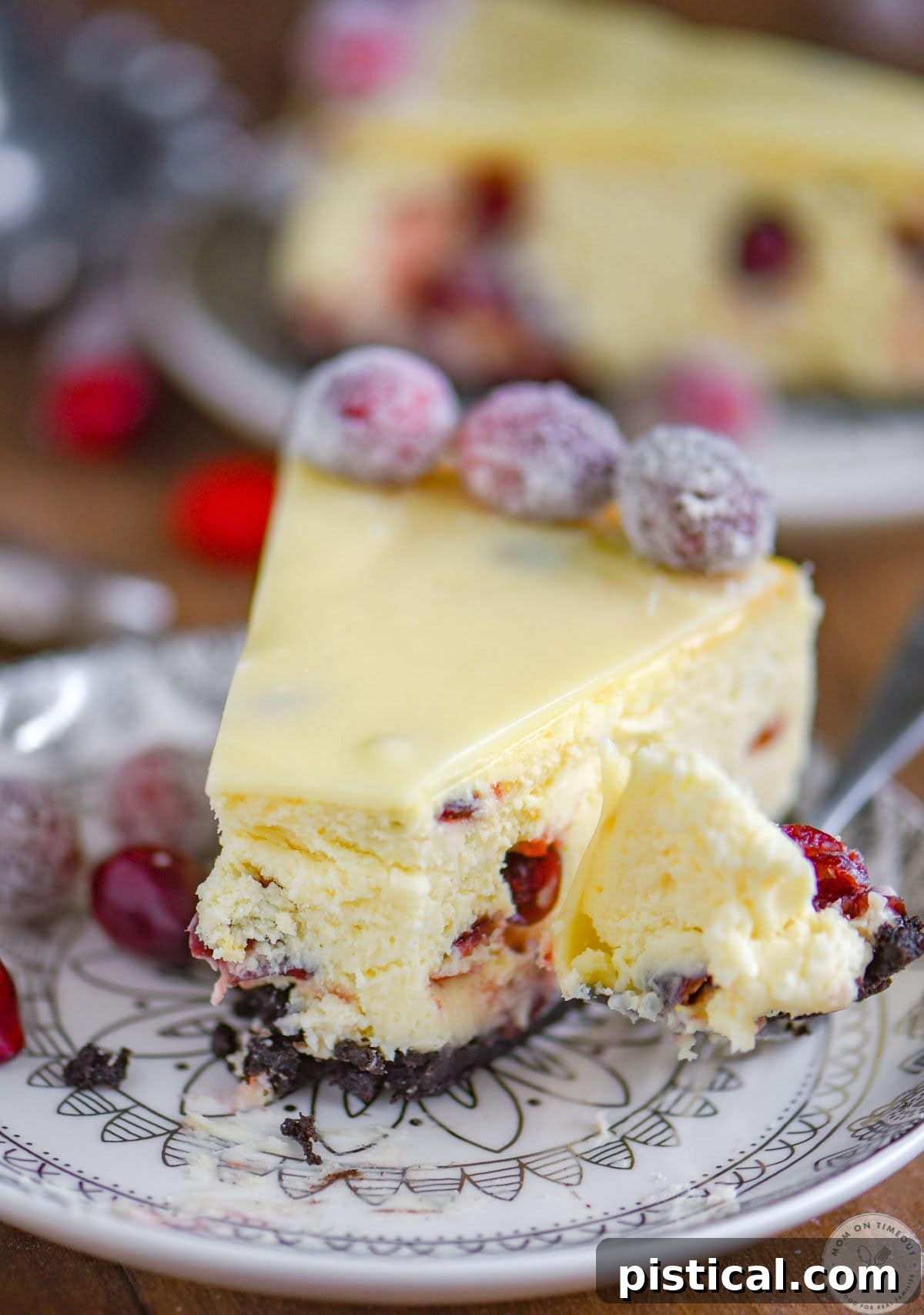 A perfectly portioned piece of white chocolate cheesecake with cranberries on a round white dessert plate, with a bite playfully taken off, highlighting its creamy texture and rich filling.