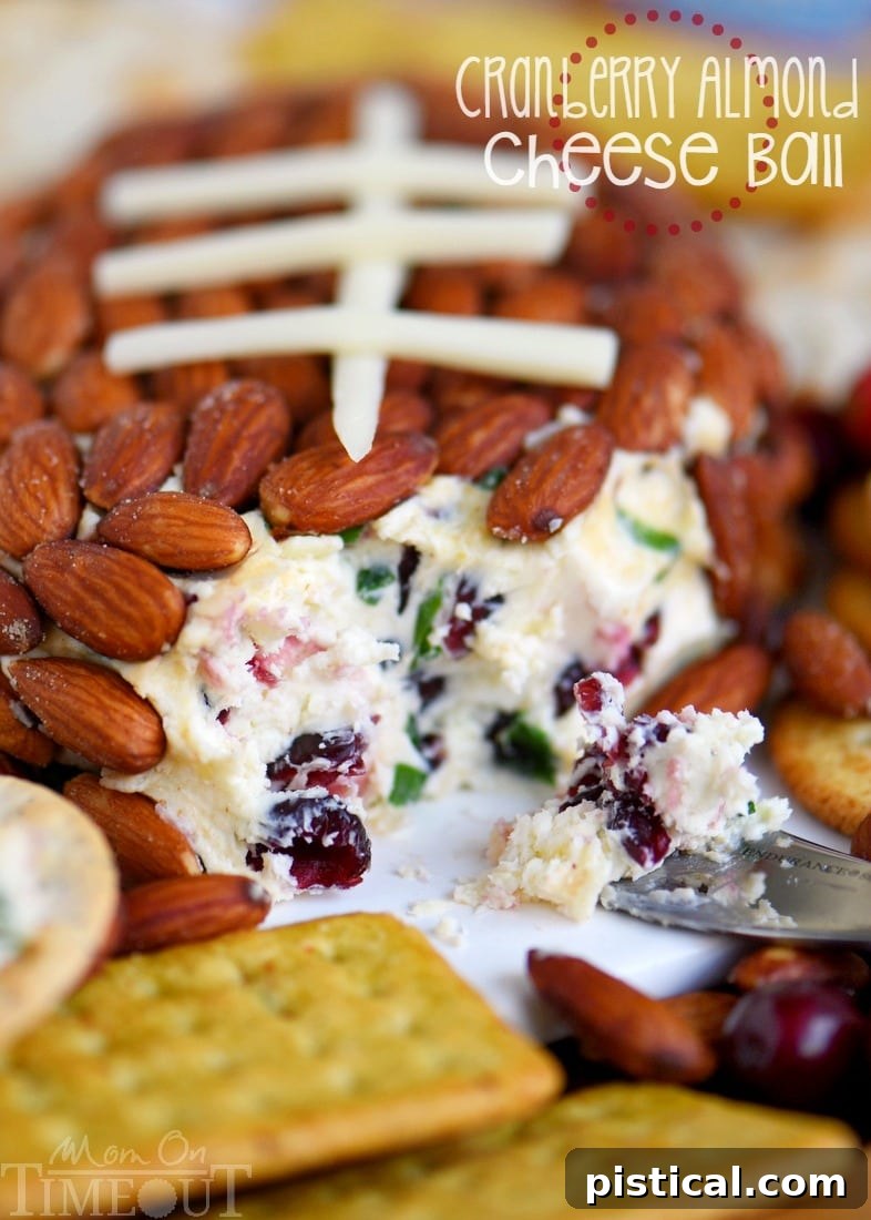 A close-up of the Cranberry Almond Cheese Ball being served on a plate, showing the creamy interior and crunchy almond exterior.