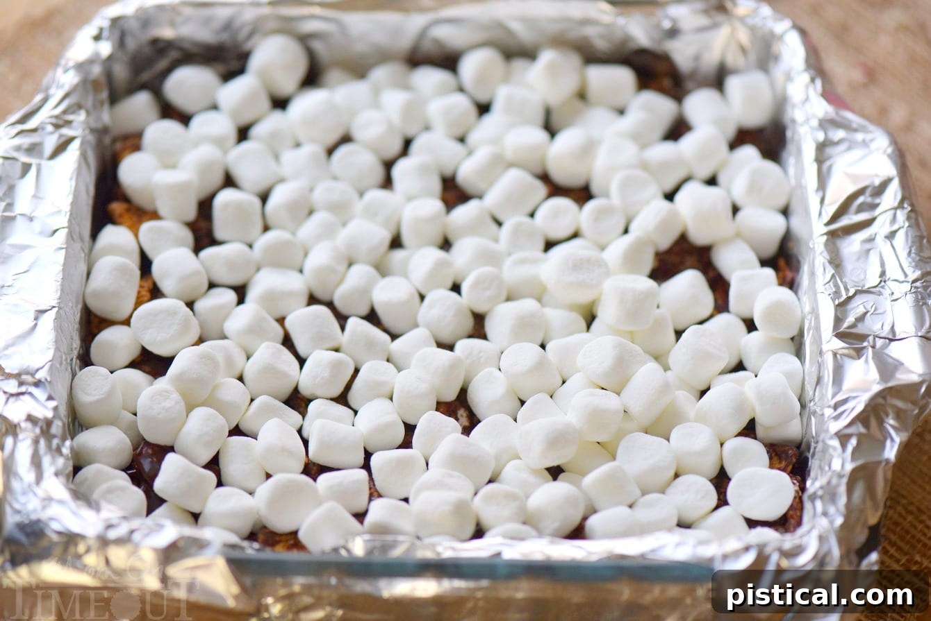 A baking pan filled with S'mores Cereal Bars, topped with a layer of miniature marshmallows, just before being placed under the broiler.