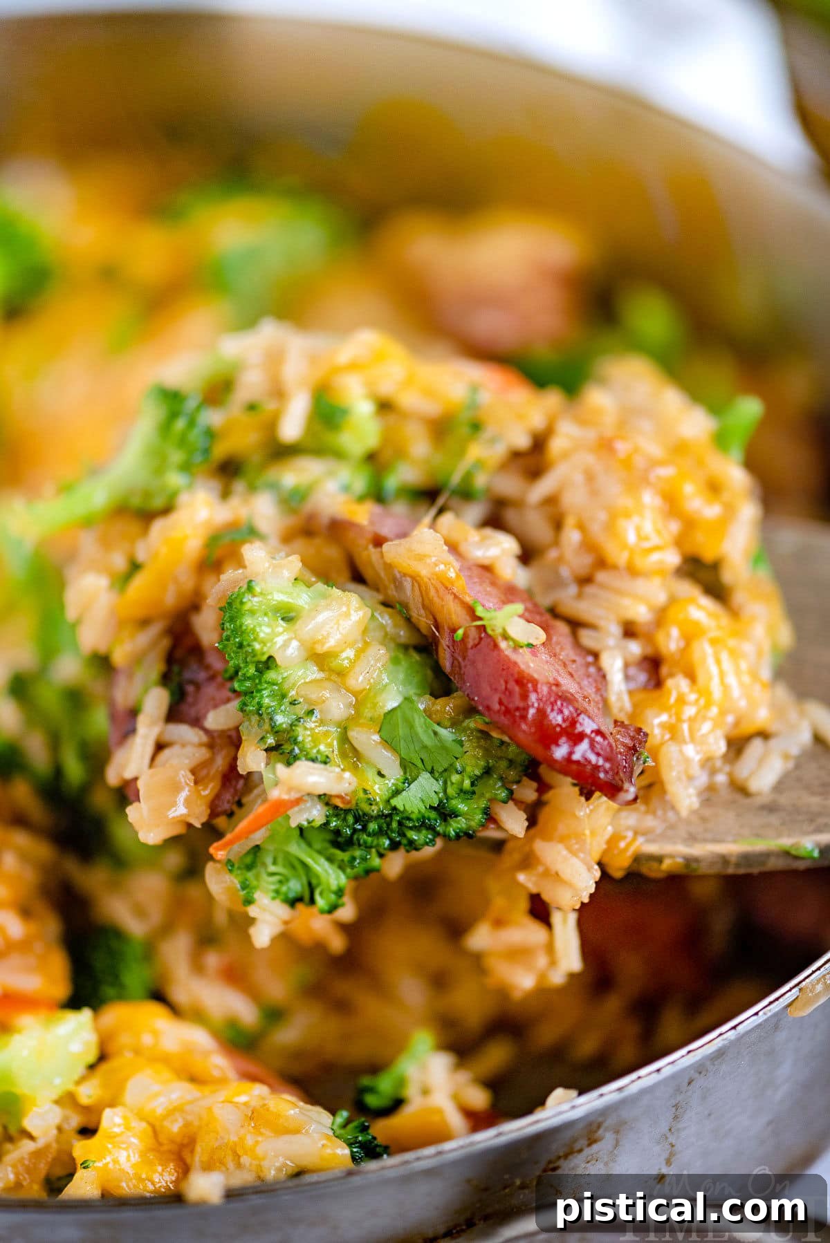Hearty Cheesy Kielbasa and Broccoli Rice Skillet 2 A serving of Cheesy Kielbasa Rice and Broccoli Skillet being scooped from the pan, showcasing the melted cheese, tender kielbasa, rice, and green broccoli florets.