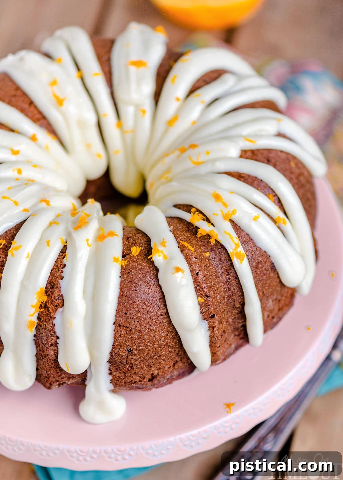 An inviting overhead, angled view of the Hummingbird Bundt Cake, generously topped with creamy cream cheese frosting and bright orange zest, beautifully highlighting its intricate texture and vibrant garnishes.