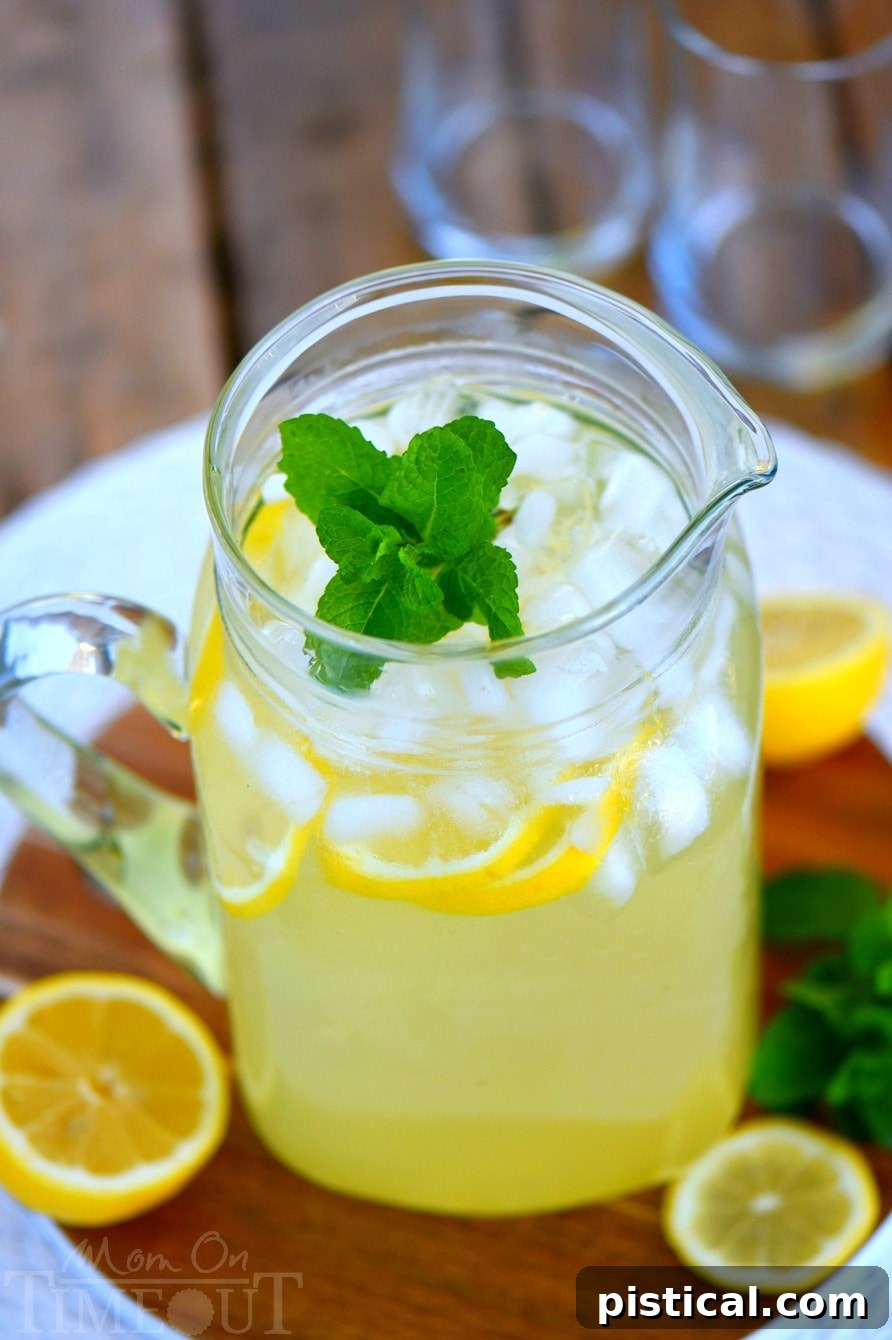 A close-up shot of a pitcher filled with Party Perfect Mint Lemonade, garnished with lemon wedges and mint sprigs.