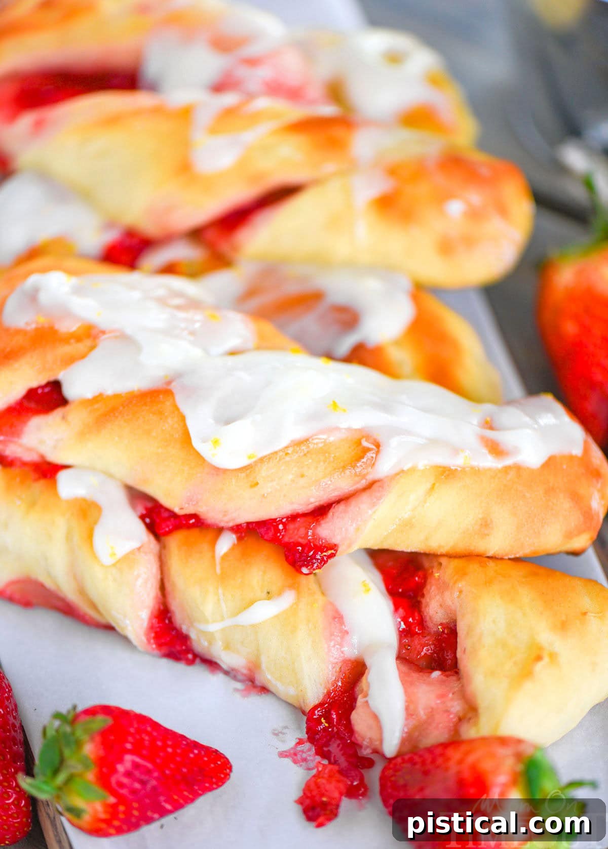 Ruby Ripple Twists 6 Two richly glazed Strawberry Twists stacked atop each other, with vibrant fresh strawberries nestled beside them, showcasing the pastry's beautiful interior.