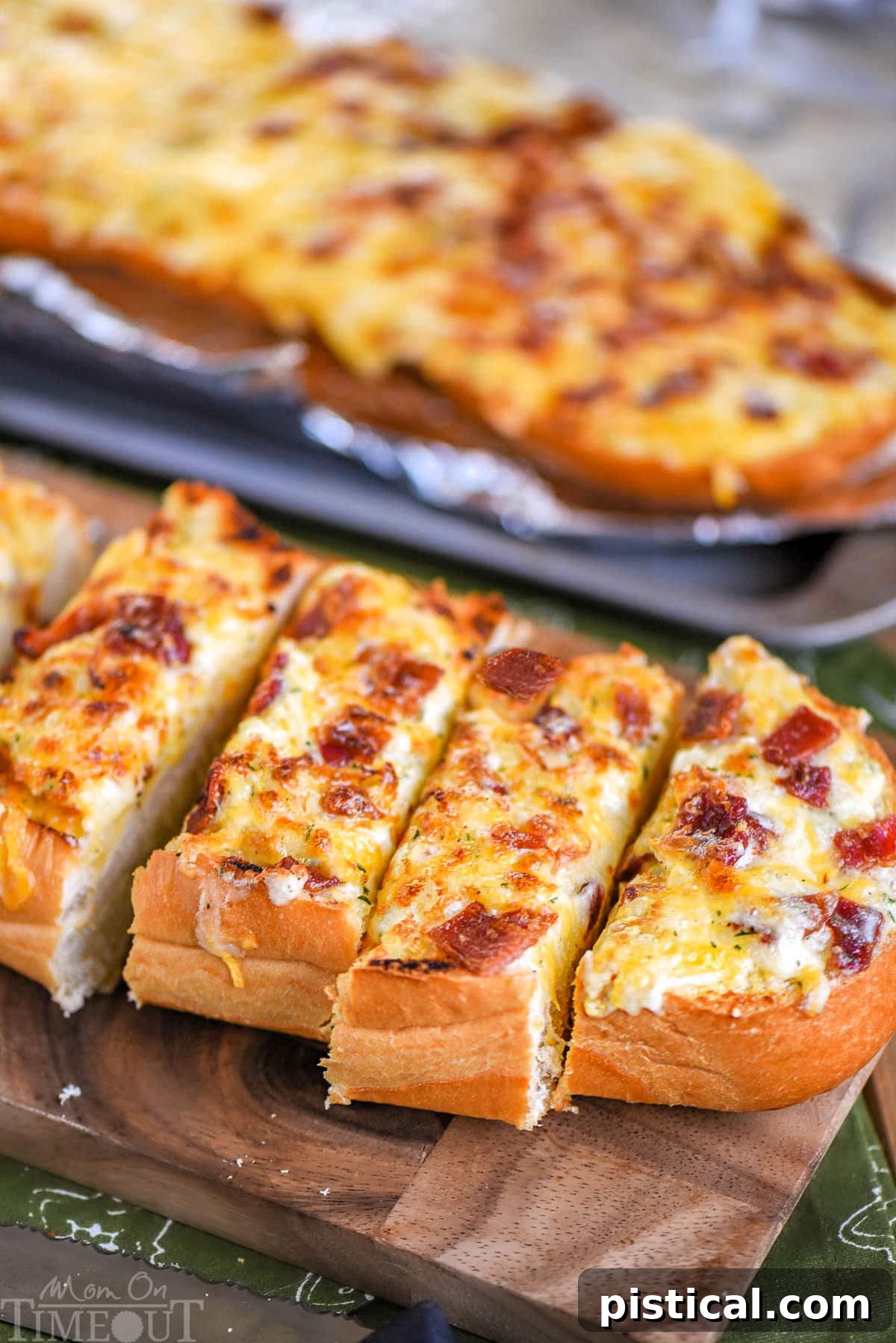 Loaf of cheesy bread made with bacon and ranch resting on wood board cut into pieces ready to be enjoyed.