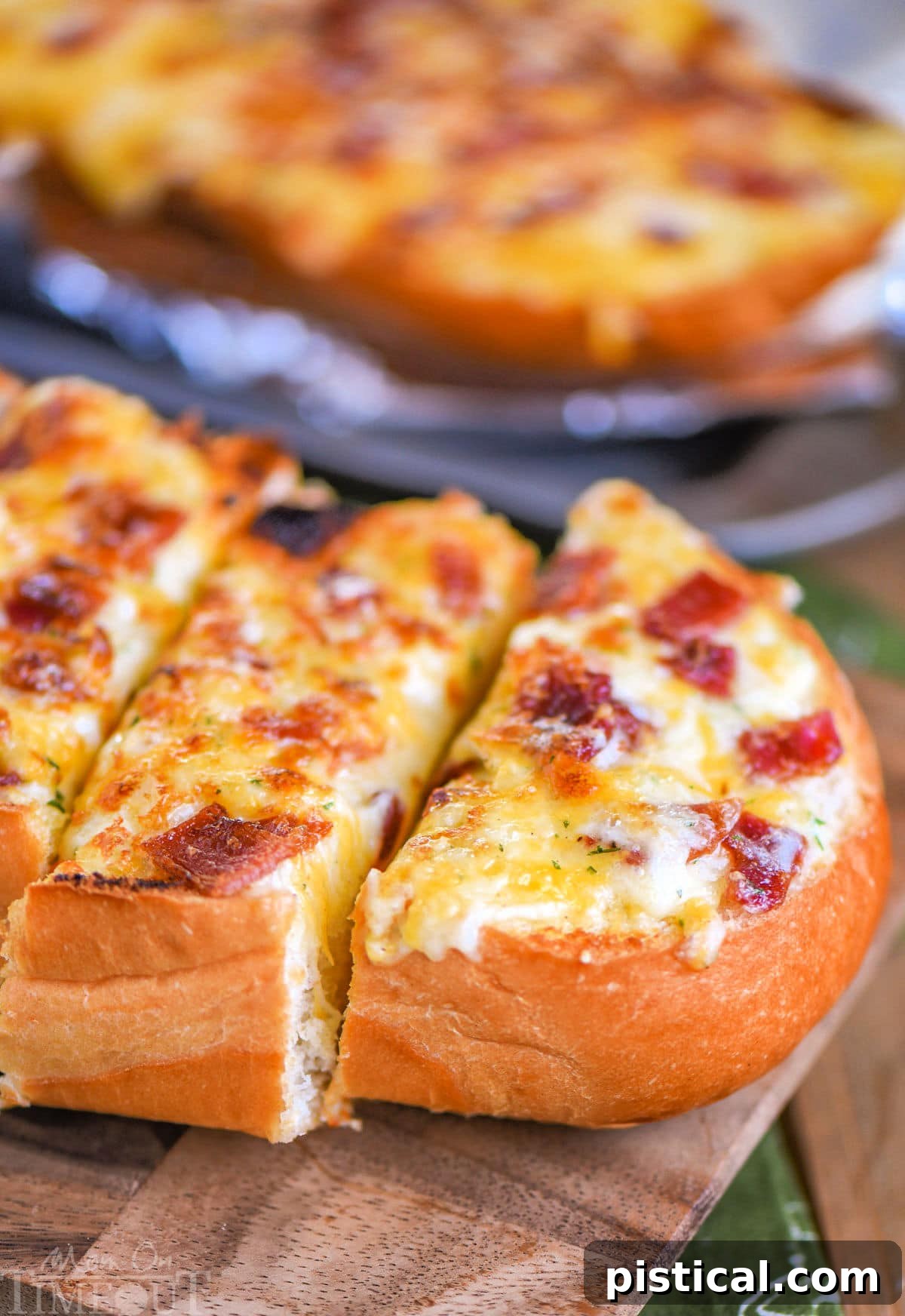 Close up look at loaf of cheese bread made with bacon and ranch. Three pieces have been cut off one half of the loaf on a wood cutting board.