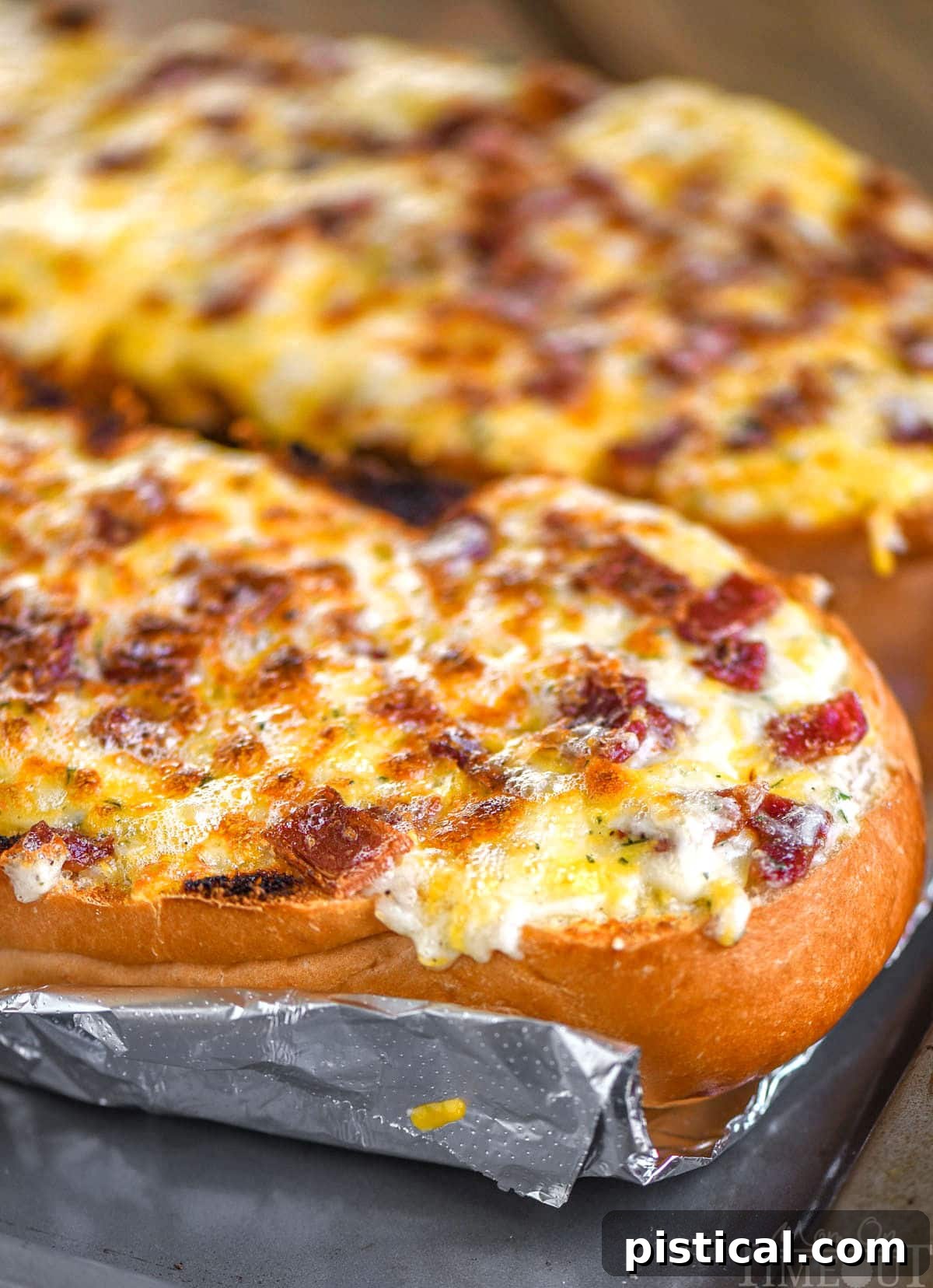 Two halves of a loaf of bread baked up into cheese bread with bacon and ranch. The bread is still on a foil lined baking sheet and has not been cut up.