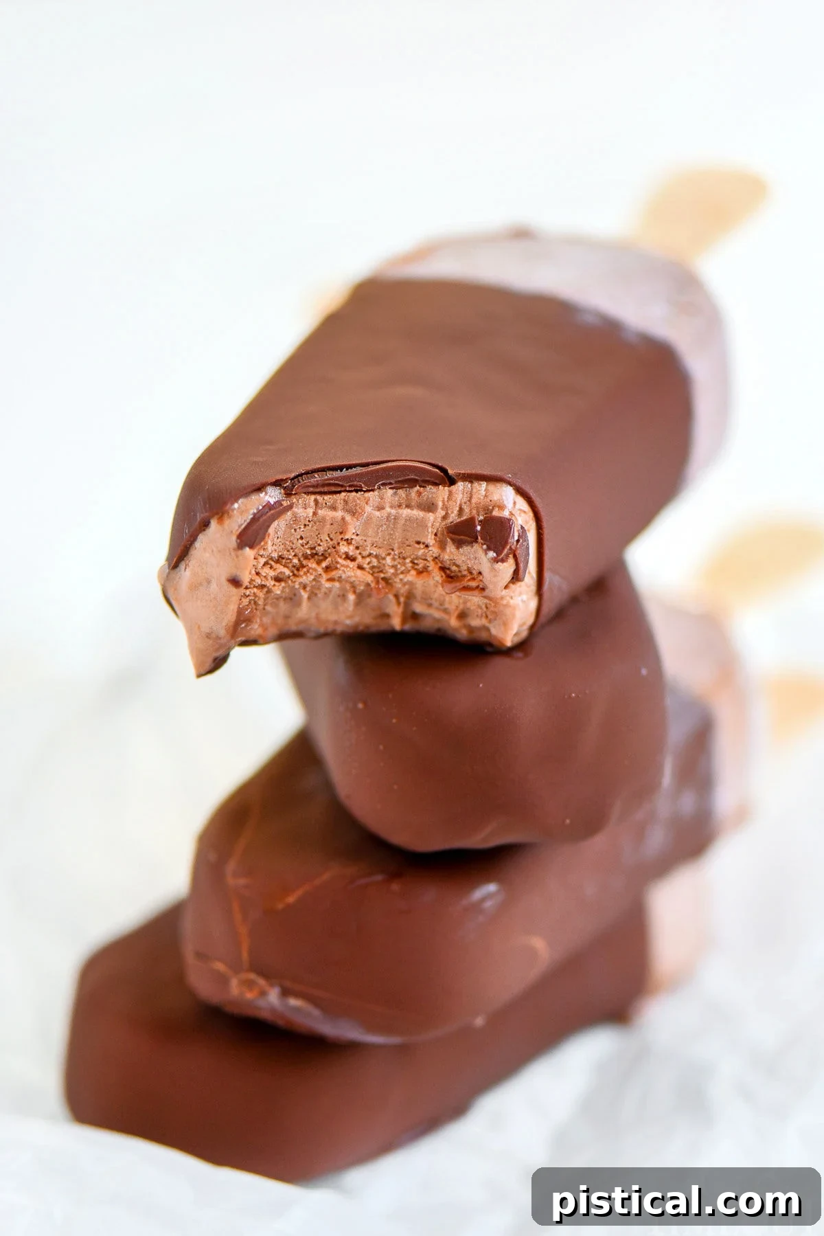 Four fudge bars that have been dipped in magic shell stacked on each other with popsicle sticks out the back.
