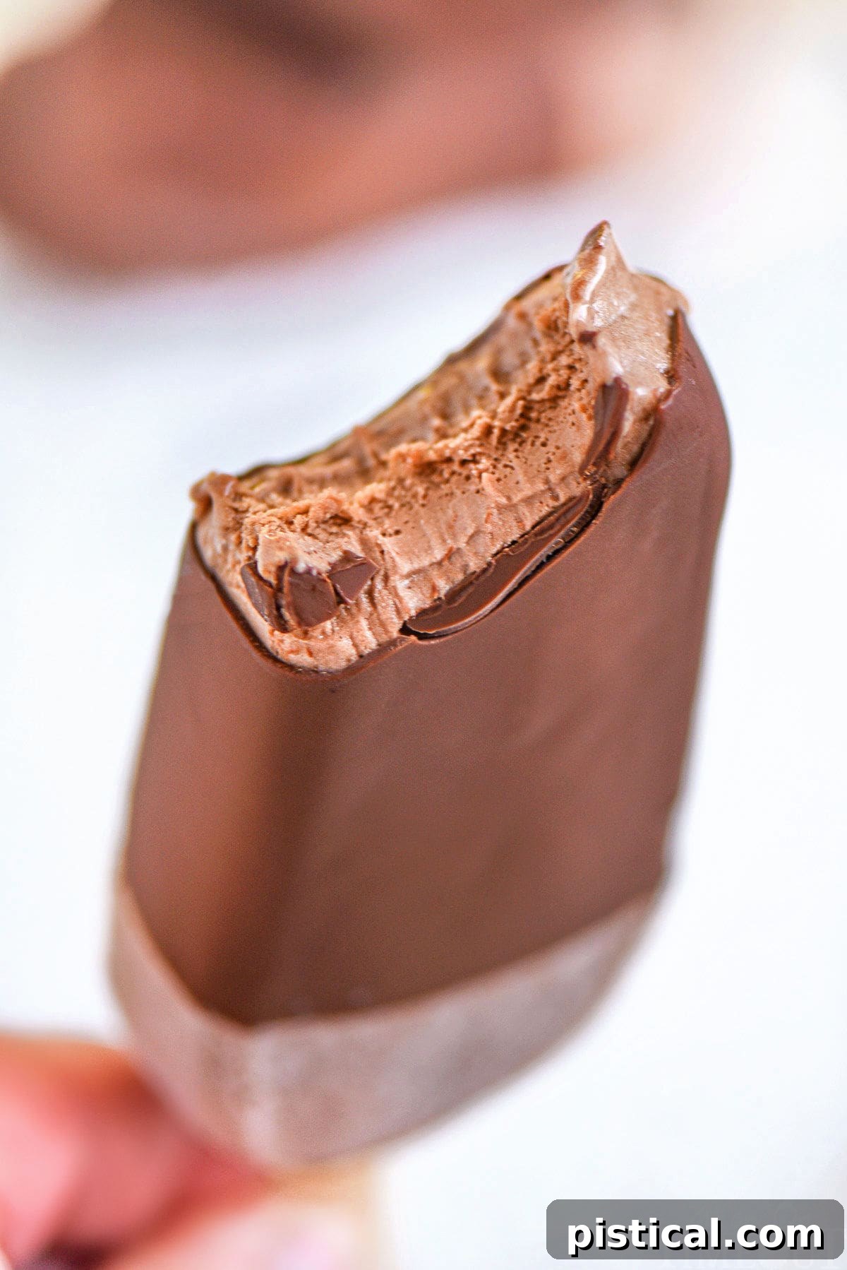 Magic shell coated fudge bar with bite taken out of it being held up.
