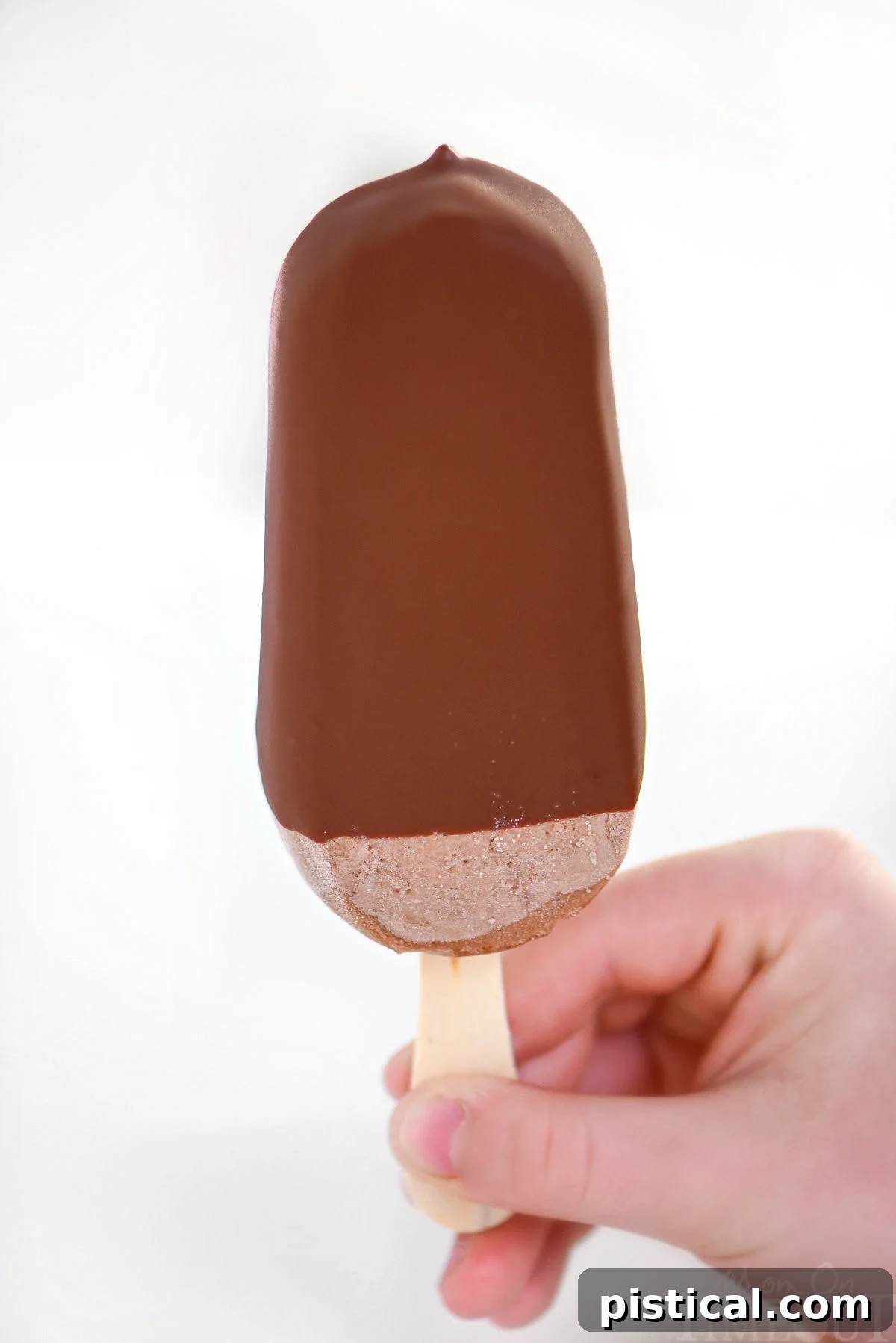 Child's hand holding up a magic shell dipped fudge pop.