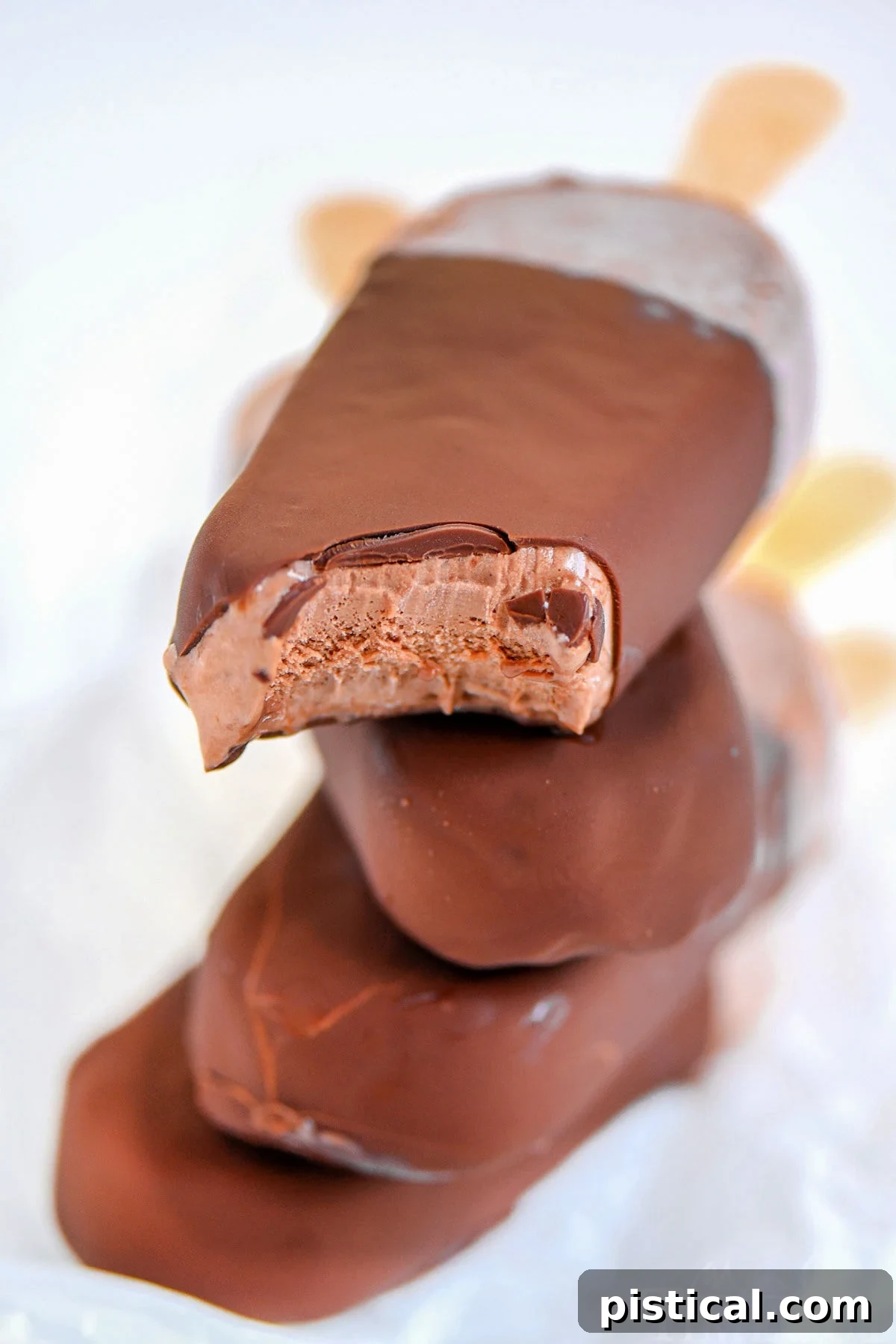 Four fudge bars that have been dipped in magic shell stacked on each other with popsicle sticks out the back.