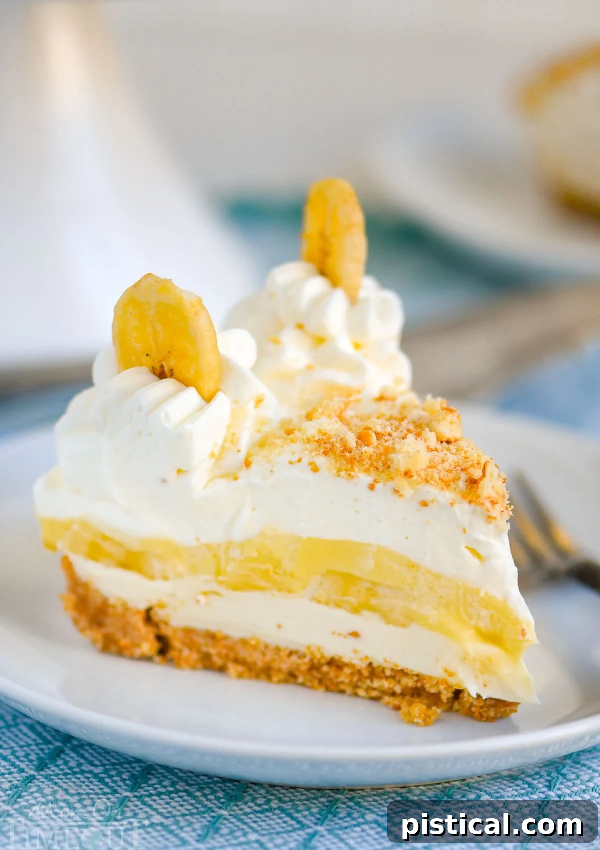 Velvet Banana Pudding Cheesecake 3 Slice of no bake banana pudding cheesecake on white round plate sitting on blue napkin.