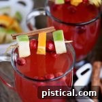 A small image of a glass of spiced cranberry apple citrus cider, garnished with fruit and cinnamon, illustrating the final festive beverage.