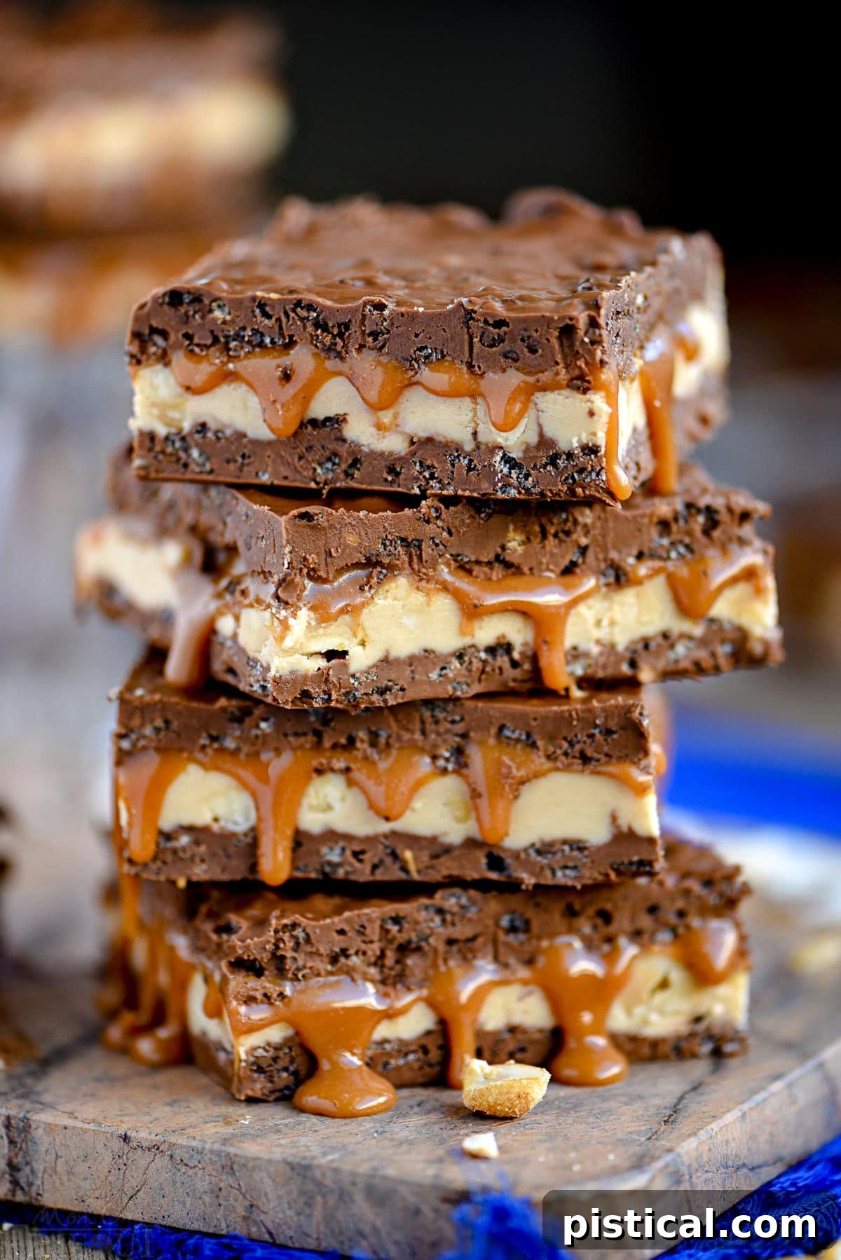 Four no-bake Snickers bars stacked on a marble cutting board, resting on a blue napkin.