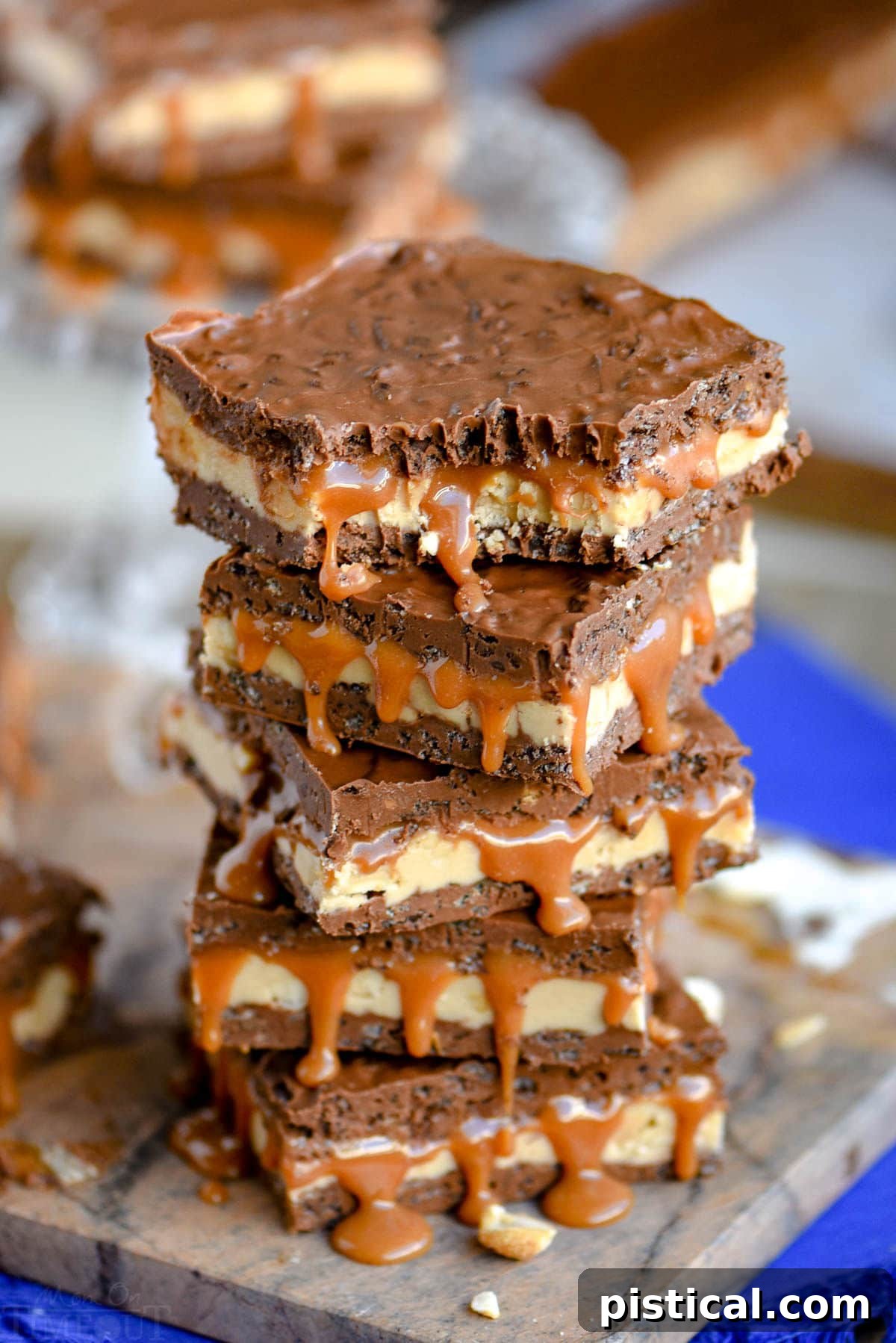 A stack of homemade Snickers bars, showing the distinct layers of crispy chocolate, nougat, and caramel. The top bar has a bite taken out of it.
