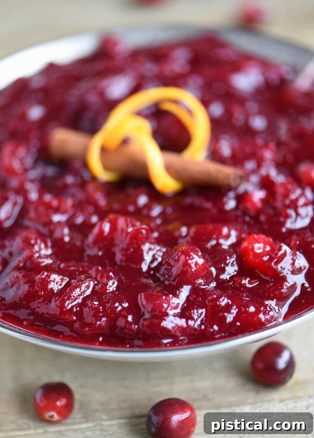 A bowl of homemade cranberry sauce, perfectly set, with fresh cranberries and orange zest scattered around, ready for serving.