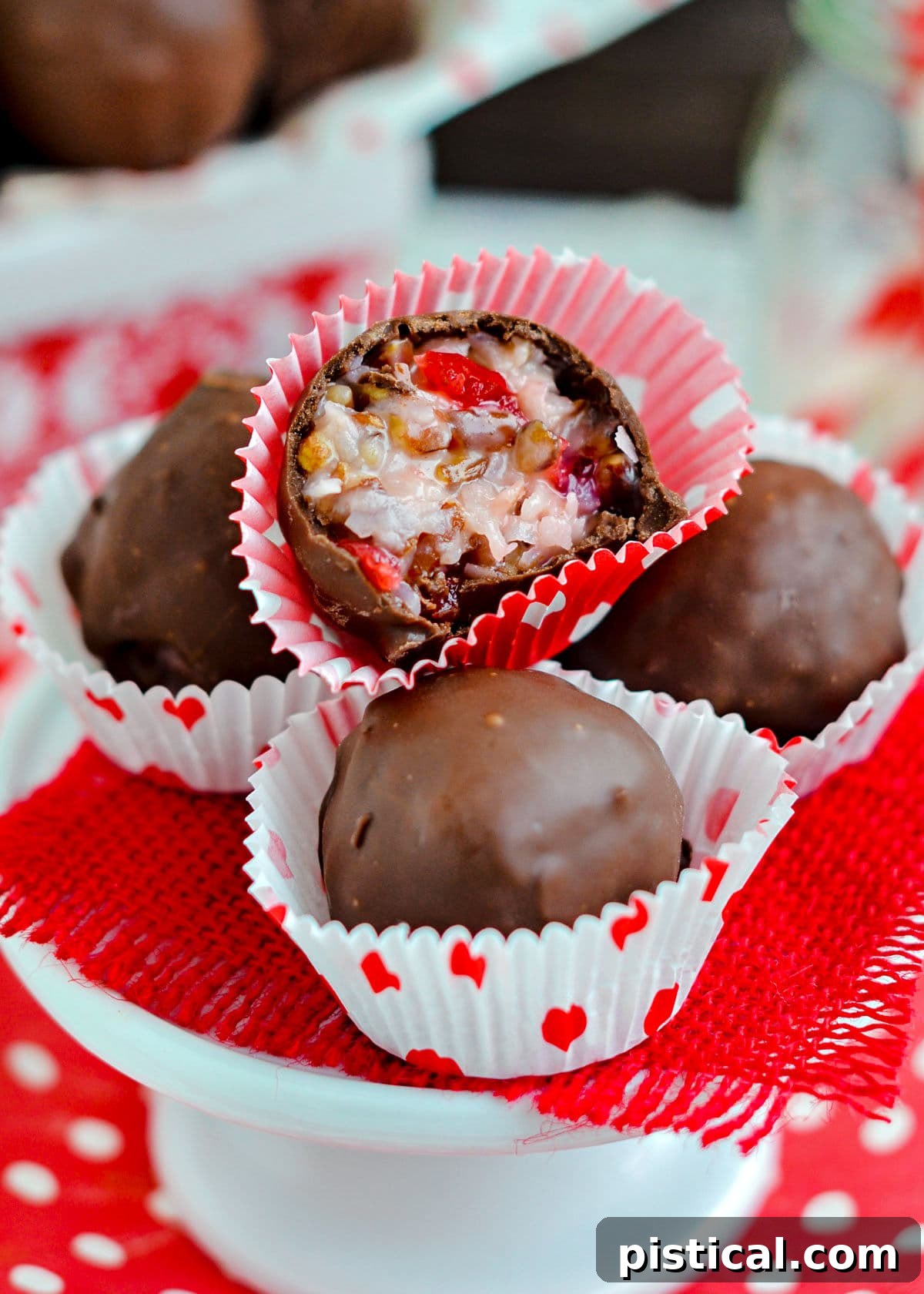 Four Martha Washington Candies, two whole and two cut in half, showcasing their coconut and cherry interiors, on a small cupcake stand.