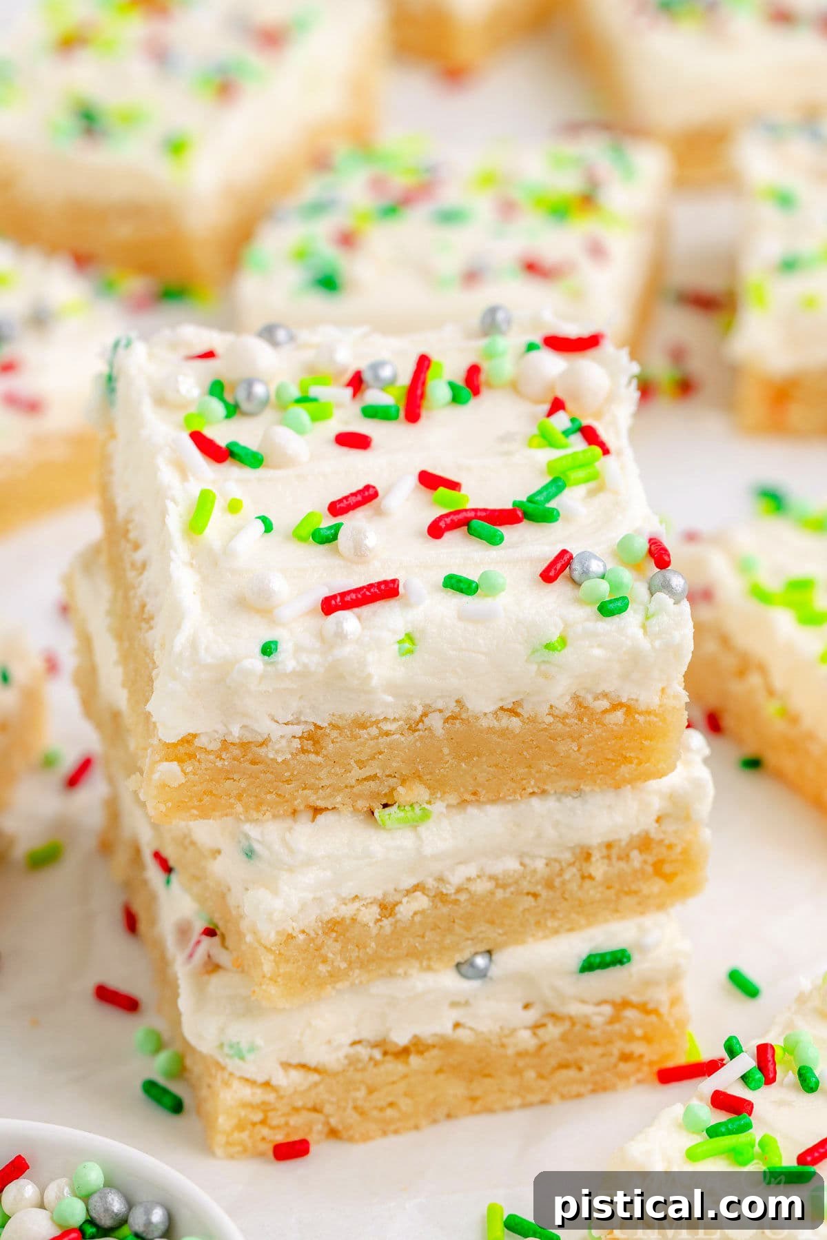A stack of three festive Christmas Sugar Cookie Bars, decorated with red and green sprinkles, with more bars in the background.