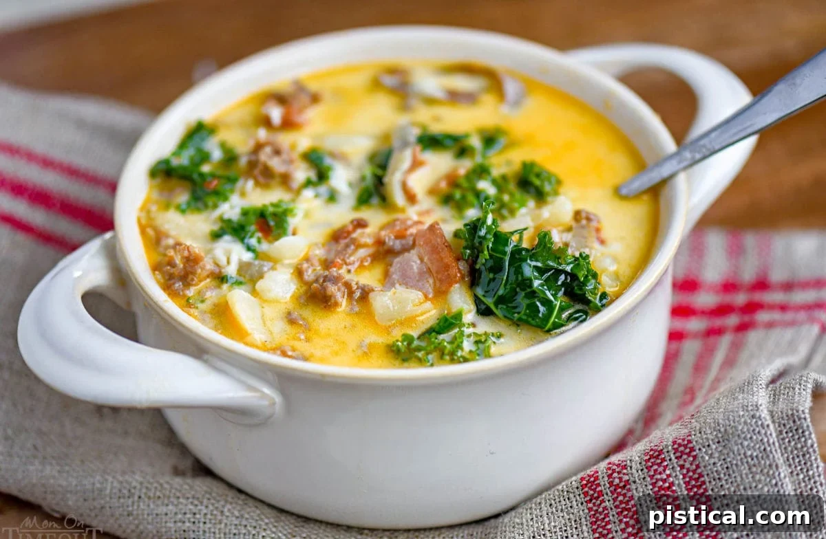 white bowl with handles filled with zuppa toscana soup and topped with cheese. Kale, sausage and bacon can be seen in the soup.