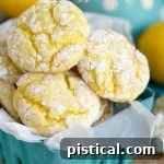 A small green basket lined with parchment paper holds several freshly baked lemon cookies, showing their crinkled powdered sugar tops.