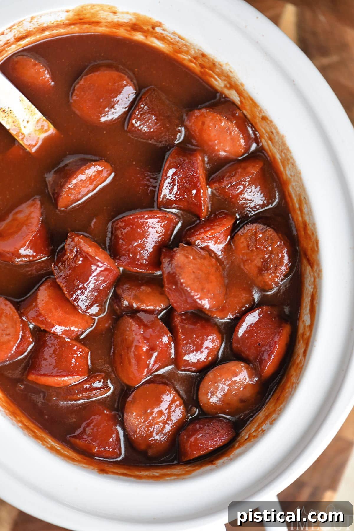 Top down look at white slow cooker full of kielbasa in a sauce made of chili sauce, bbq sauce and grape jelly.