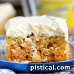Piece of pineapple cake recipe on blue and white plate topped with pineapple fluff frosting.