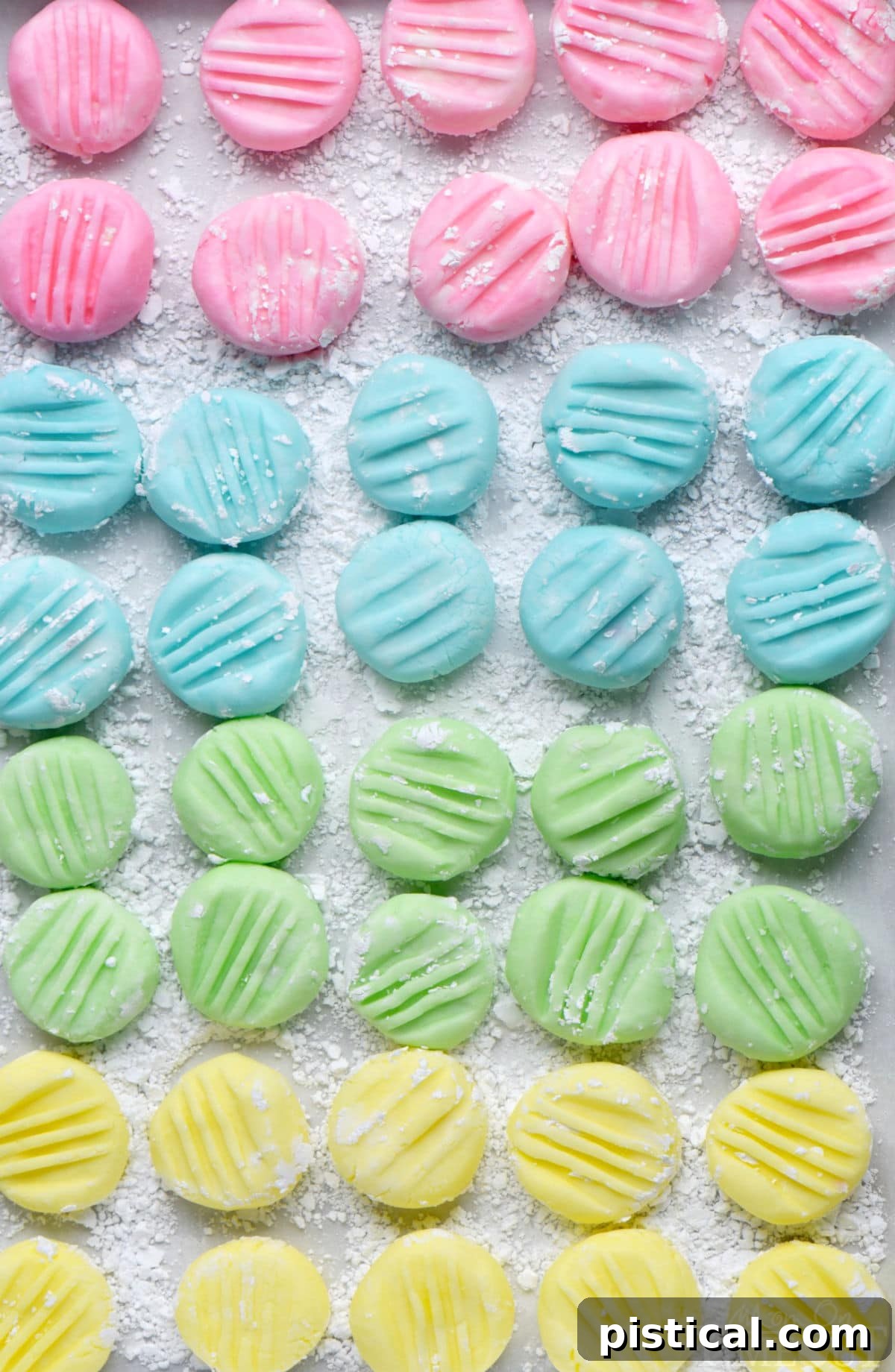 Irresistible Cream Cheese Mints 7 Top down view of recipe for cream cheese mints on parchment paper flattened with the tines of a fork. Four pastel colors are shown: pink, blue, green and yellow in a symmetrical grid layout.