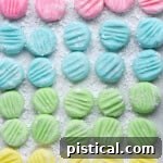 Irresistible Cream Cheese Mints 8 Top down view of recipe for cream cheese mints on parchment paper flattened with the tines of a fork. Four pastel colors are shown: pink, blue, green and yellow in a symmetrical grid layout.