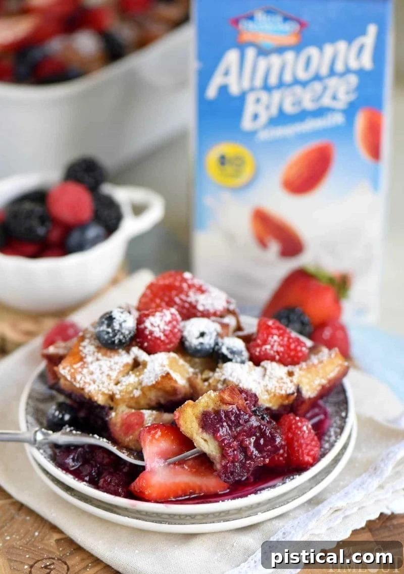 Ingredients for Triple Berry French Toast Casserole laid out on a table: French bread cubes, eggs, almond milk, vanilla, cinnamon, sugar, and mixed frozen berries.
