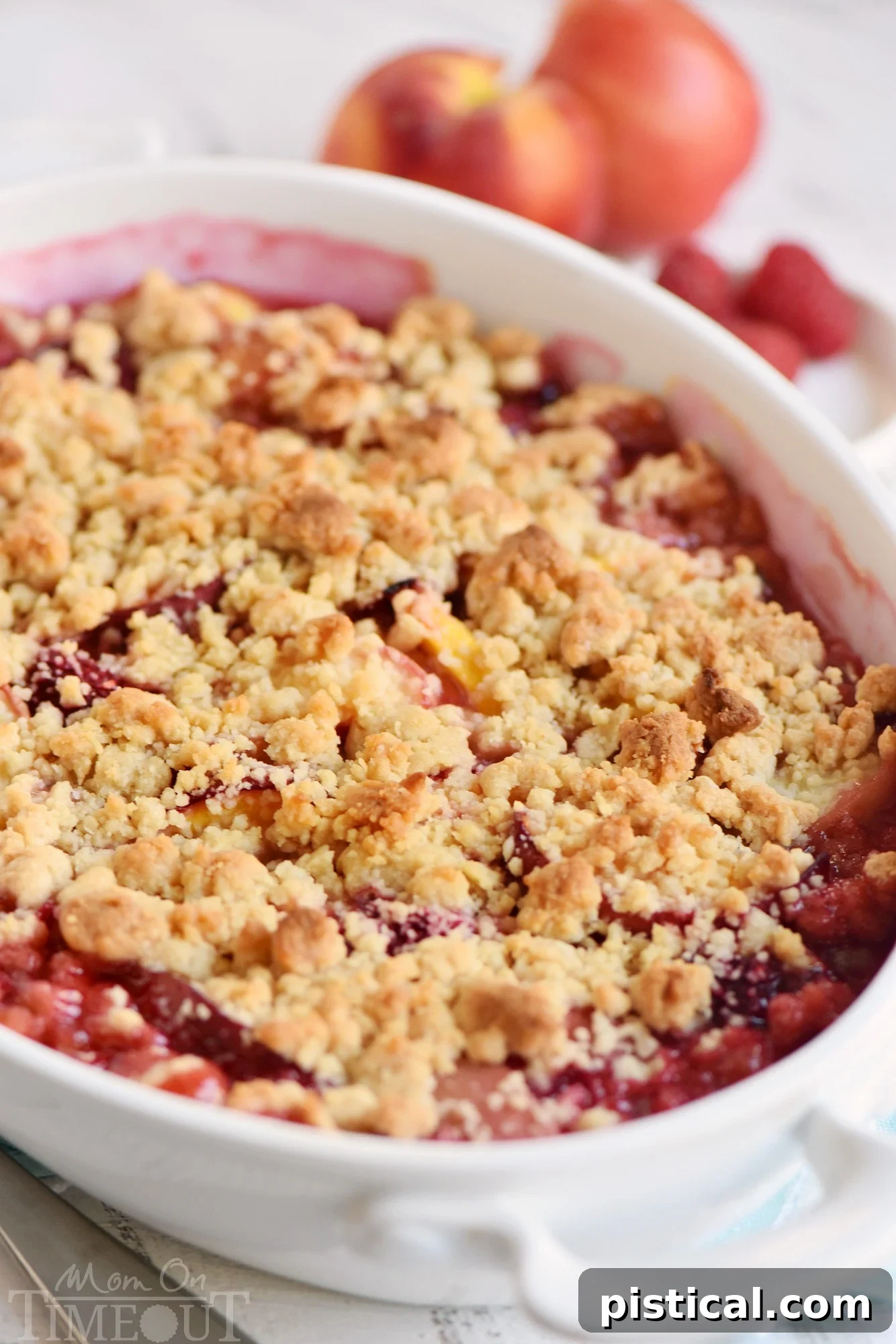 Close-up of unbaked Raspberry Peach Crumble in a baking dish, showing the colorful fruit filling topped with a textured brown sugar crumble