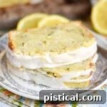 Two slices of lemon zucchini loaf cake stacked on each other on small white plate. cake has a a lemon glaze on the top.