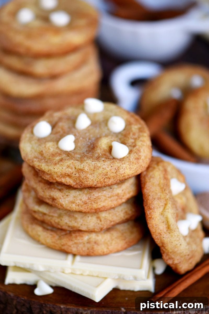 A stack of three White Chocolate Snickerdoodles resting on white chocolate squares, showcasing their soft centers and melted white chocolate chips.