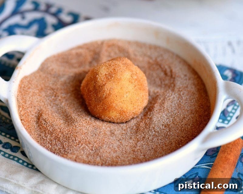 A child's hands gently rolling a Snickerdoodle cookie dough ball in a bowl of cinnamon sugar, preparing it for baking.