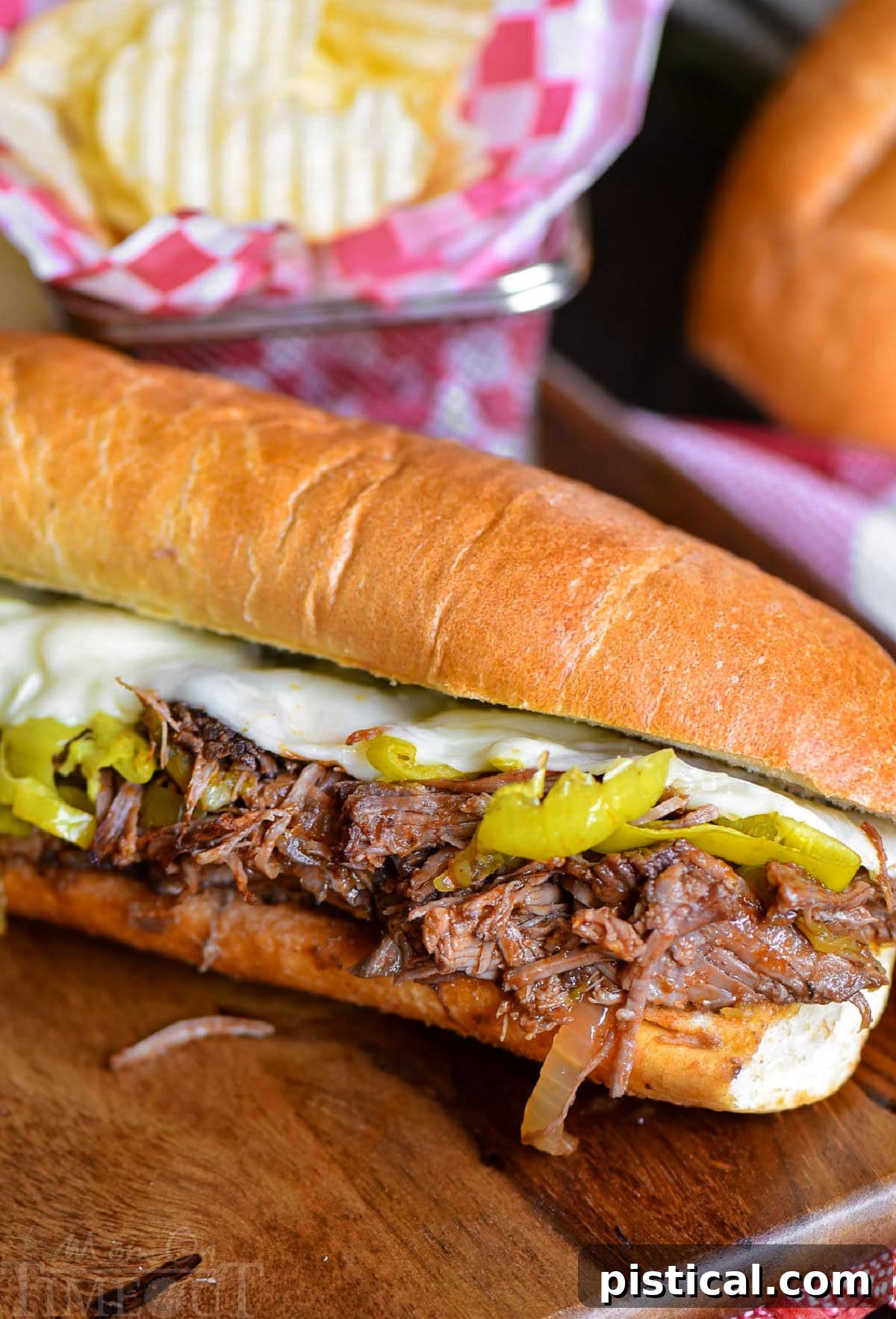 Fall-Apart Tender Slow Cooker Italian Beef Sandwiches 2 Italian Beef Sandwich sitting on wood cutting board with a basket of chips behind it.