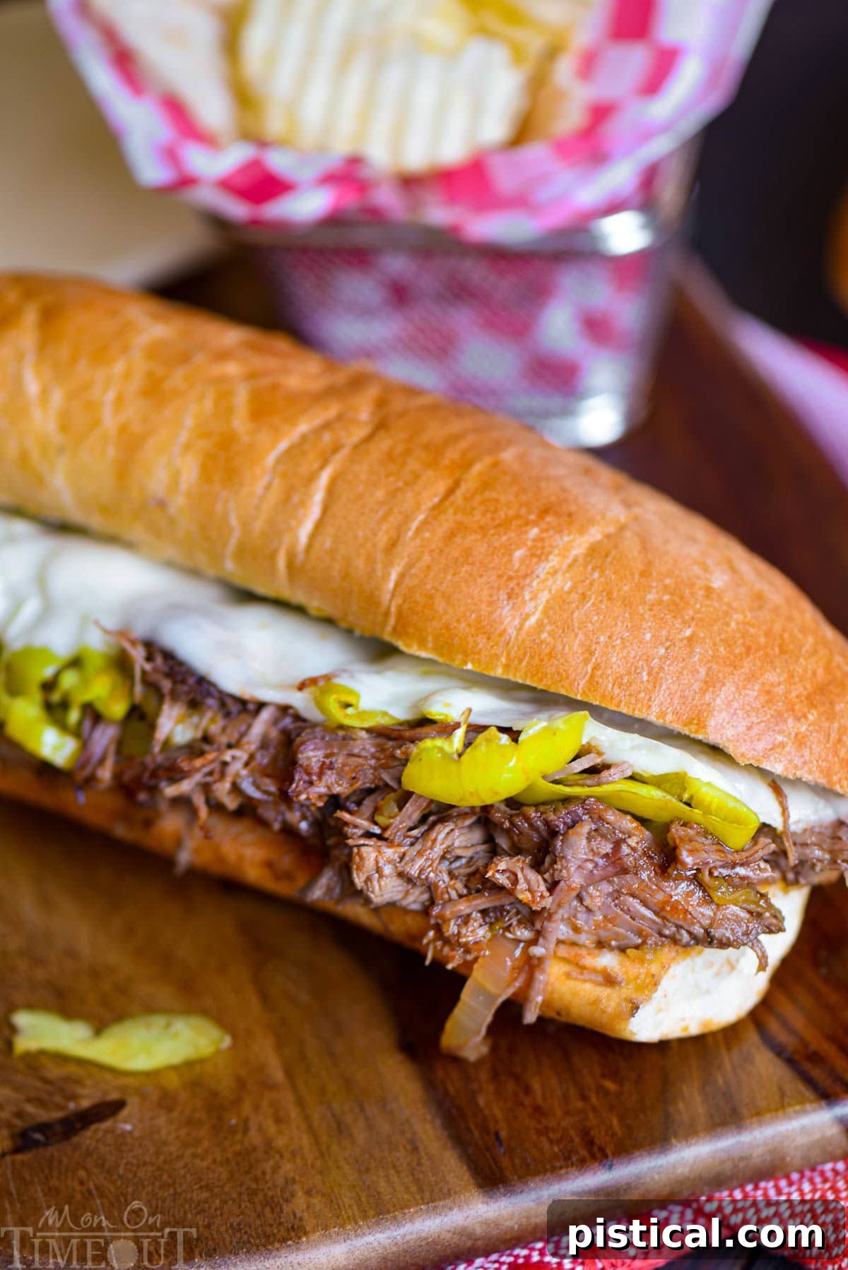 Fall-Apart Tender Slow Cooker Italian Beef Sandwiches 6 Italian Beef Sandwich recipesitting on wood cutting board with a basket of chips behind it.