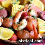 top down view of shrimp boil in serving dish made with shrimp, potatoes, corn and more. shown with lemon wedges for serving.