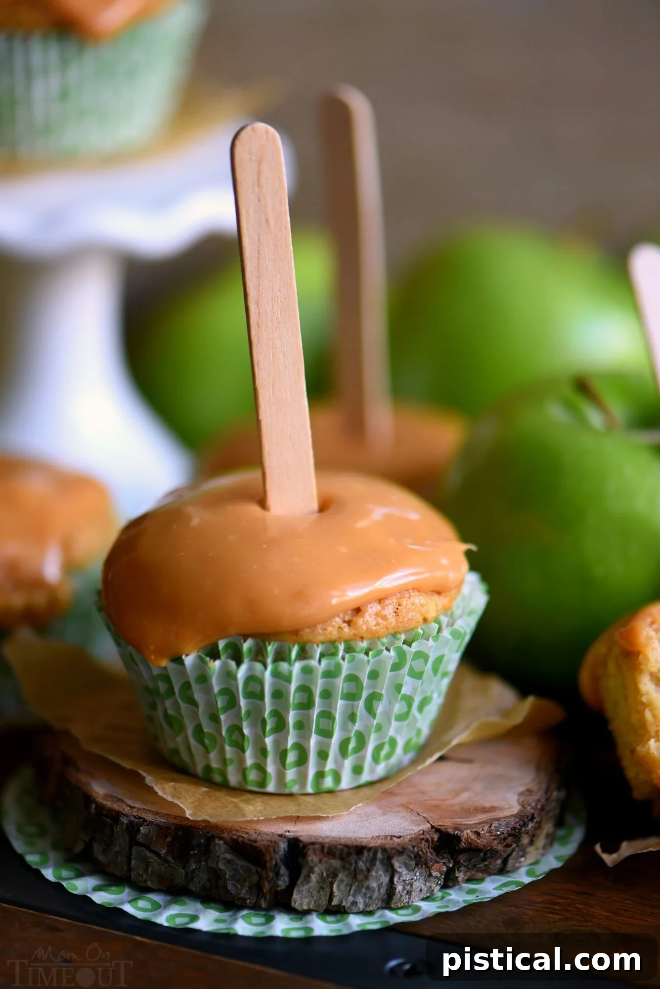 A beautifully arranged selection of Caramel Apple Cupcakes, each topped with gooey caramel frosting and a wooden popsicle stick. They are displayed on a rustic wood board, embodying the perfect fall treat. This image encourages sharing and enjoying the seasonal delights. // Mom On Timeout