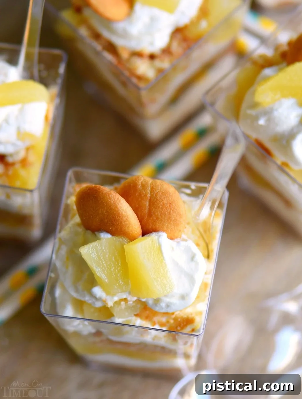 Close-up of a beautifully layered Mini Pineapple Cheesecake Trifle in a clear cup, showcasing vanilla wafers, creamy cheesecake, and pineapple.