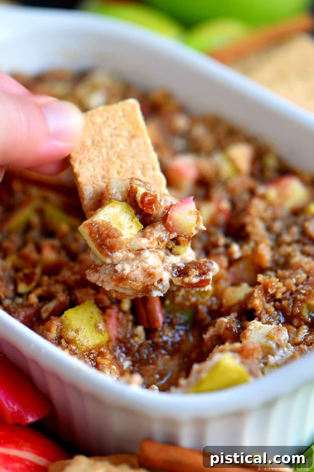 Crispy graham crackers being dipped into a warm, creamy apple pie dip, showcasing the rich texture and delicious streusel topping.