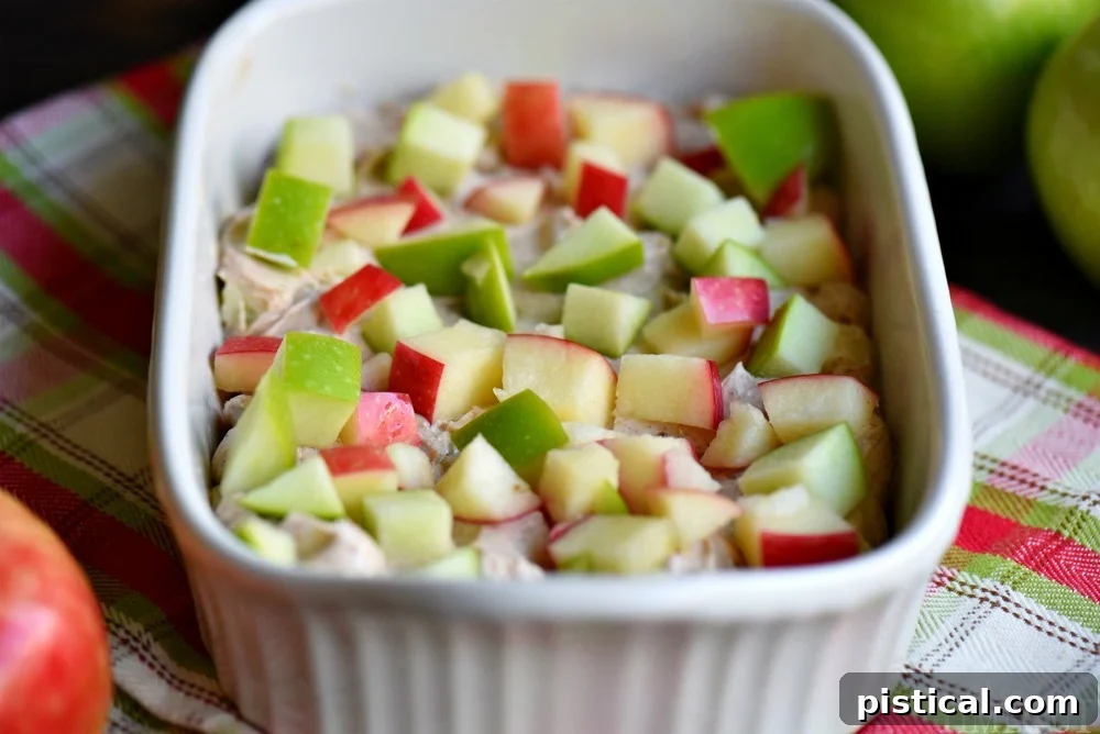 A baking dish filled with the creamy base of the apple pie dip, topped with diced fresh apples before the streusel layer is added.
