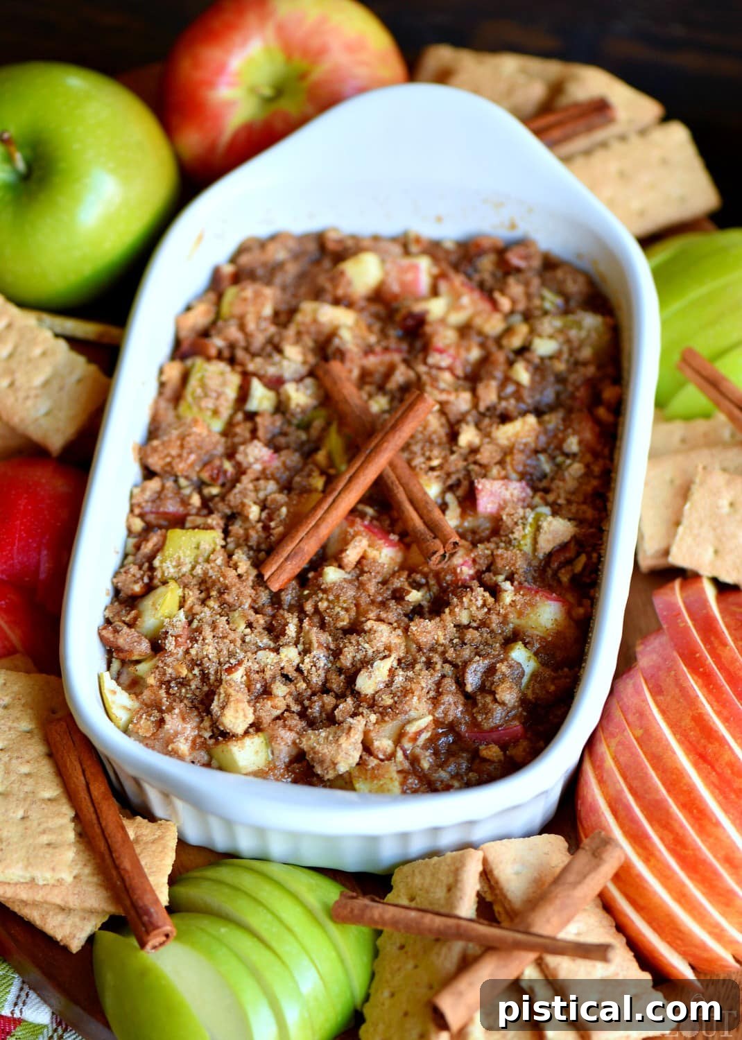 An array of dippers including apple slices and graham crackers surrounding a dish of easy baked apple pie dip on a rustic wooden board.