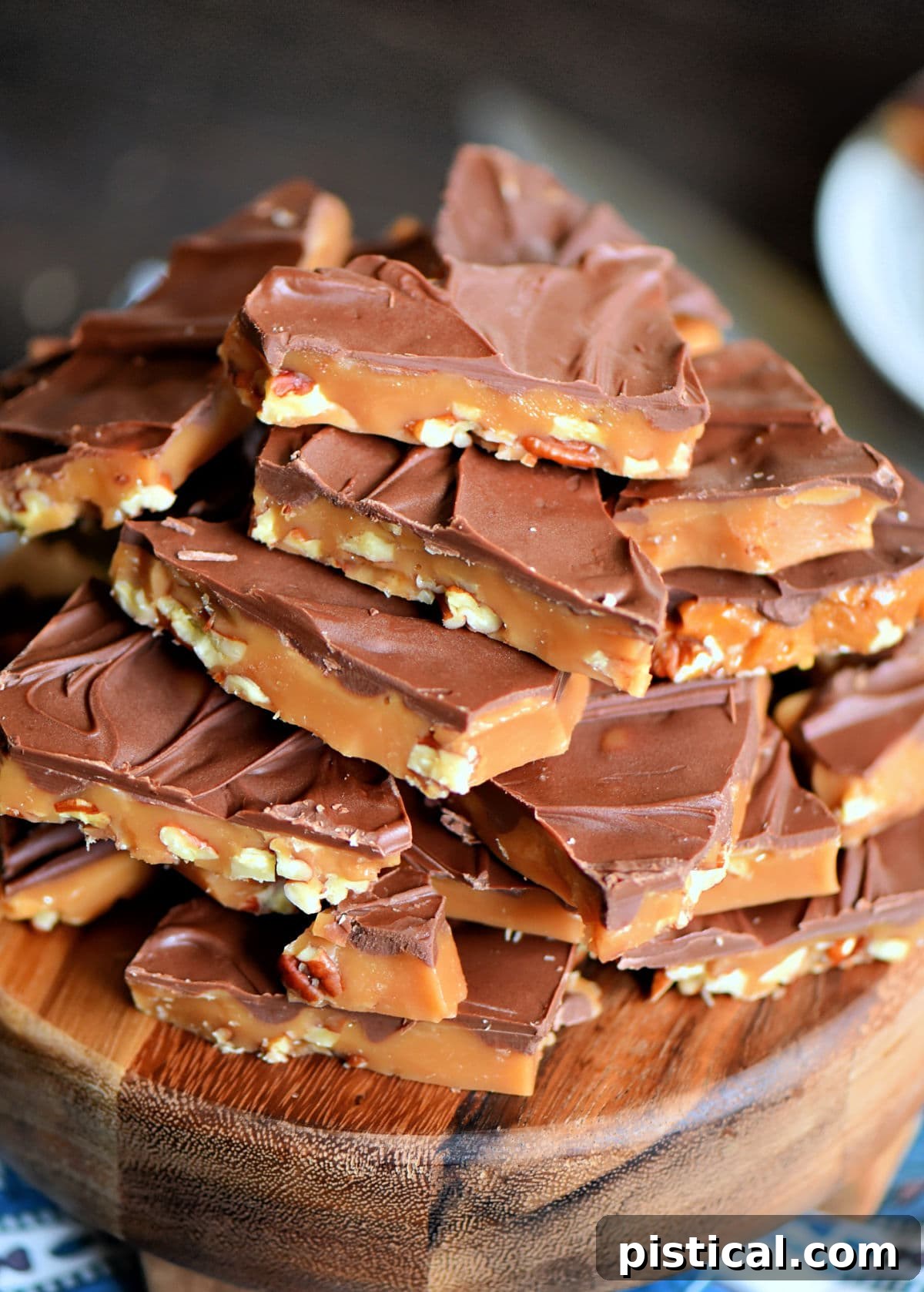 angled look at giant stack of toffee topped with milk chocolate sitting on a round wood board ready to be enjoyed.