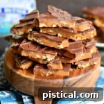 broken up toffee topped with chocolate sitting on a small round wood serving board.