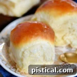 Two fluffy dinner rolls sitting on a round white plate with gold trim.