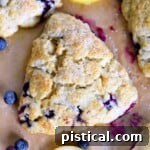 Zesty Lemon Blueberry Scones 8 top down view of lemon blueberry scone on a piece of brown parchment paper with fresh blueberries scattered about.