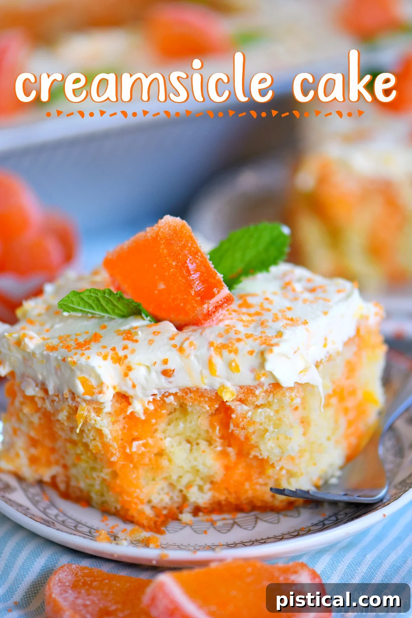 A perfectly sliced piece of Orange Creamsicle Poke Cake, garnished with fresh mint leaves, resting on a small white plate with a fork beside it. The cake shows distinct orange and vanilla layers.