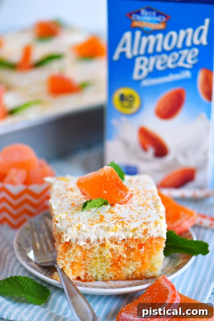 A close-up of a single slice of Orange Creamsicle Poke Cake on a small white plate, adorned with mint leaves, showing the delightful orange Jell-O streaks and fluffy frosting. Candied orange slices are visible on top of the cake.