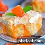slice of creamsicle cake on round white plate topped with fluff frosting and orange candy.